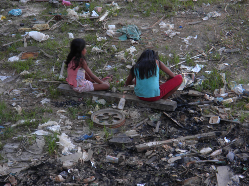 Young girls sitting in trash in an inlet of the Rio Negra